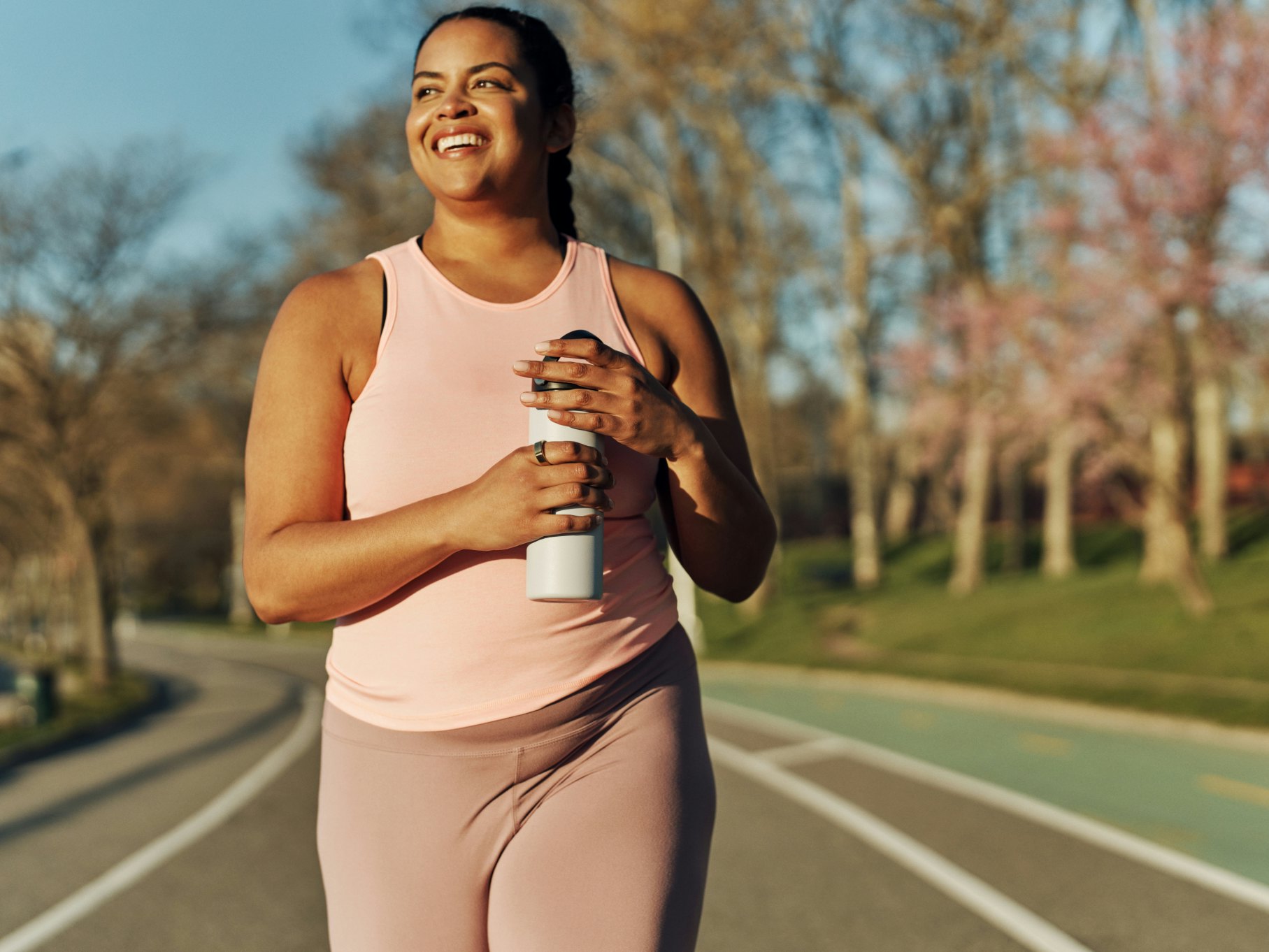 Woman wearing an Oura Ring and holding a water bottle while walking on a track