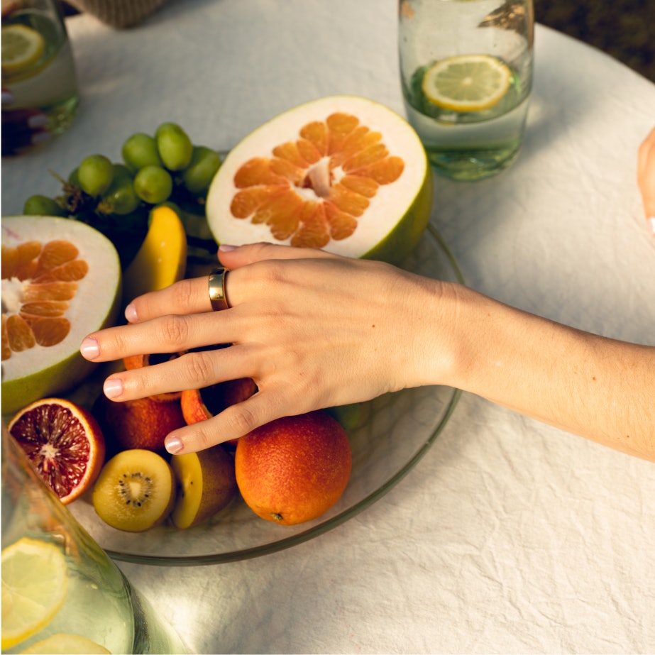 A hand over a fruit platter with an Oura ring on their index finger.
