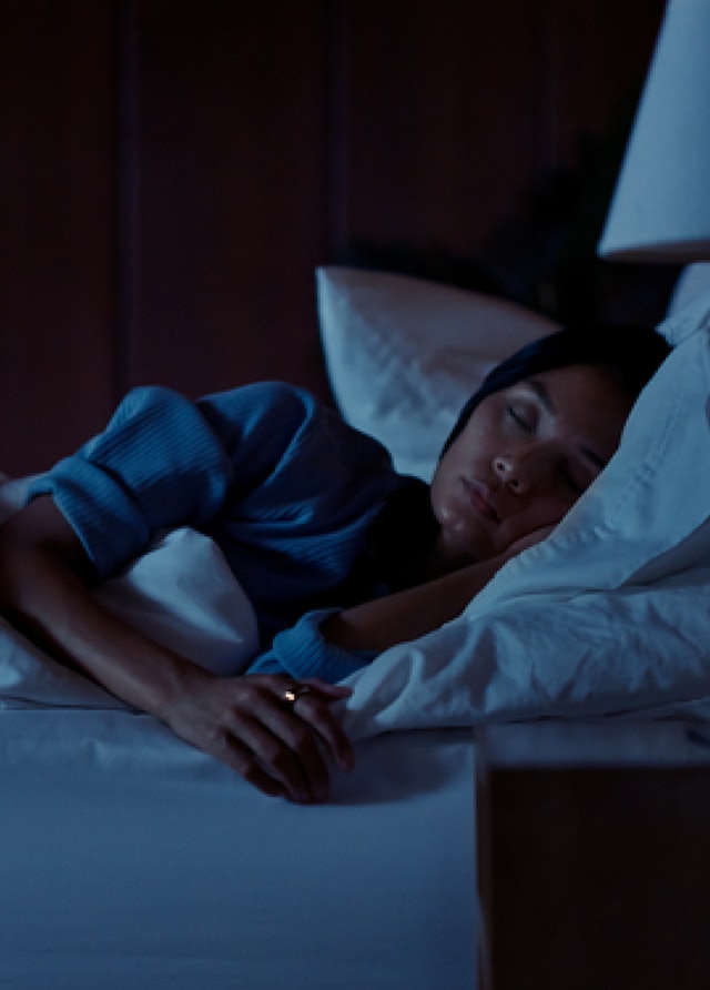 Une femme dort dans un lit, l'anneau Oura Gold à l'index droit