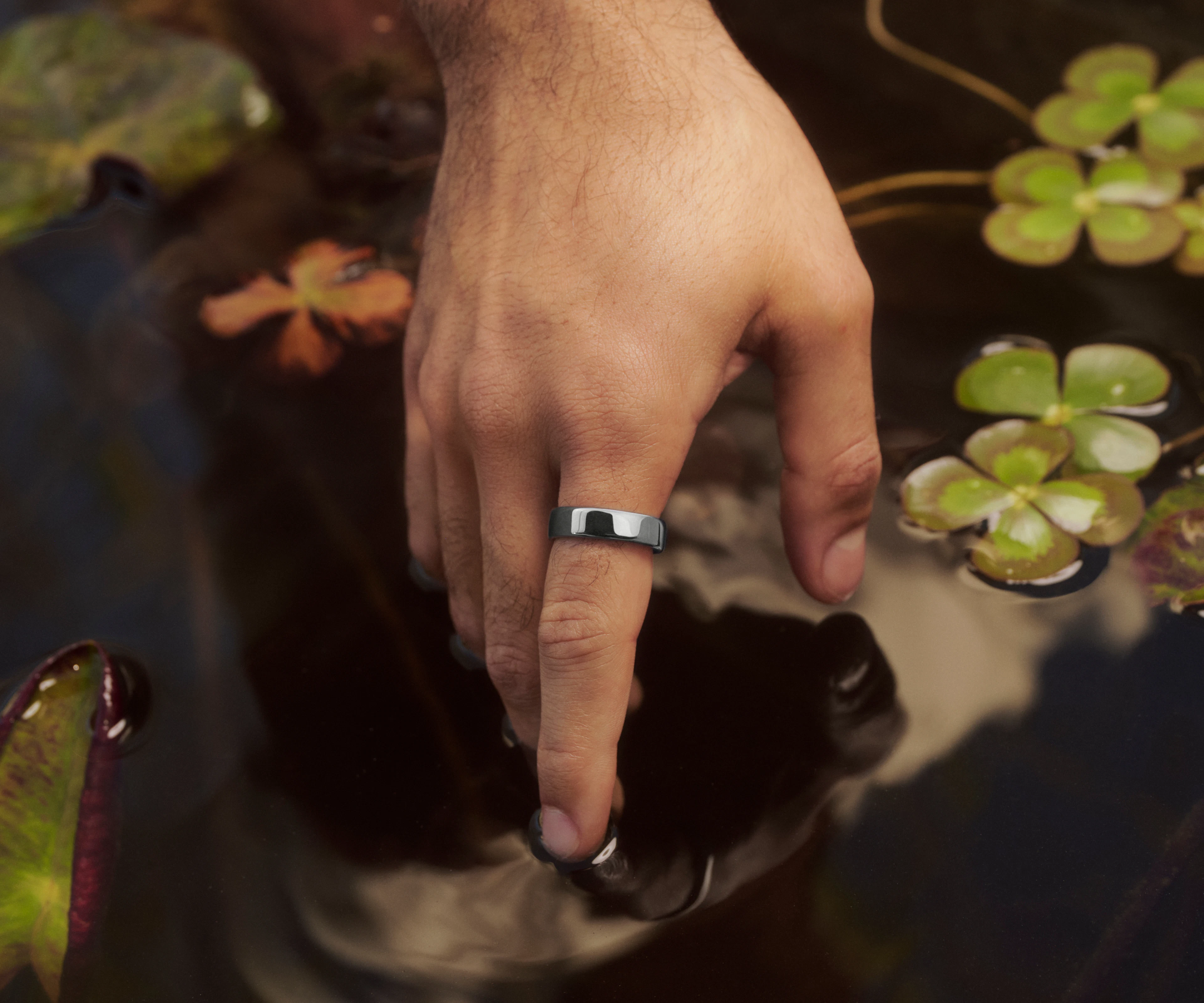 SilverのOura Ring 5を着用し、観賞用の池の水面を触っている手のクローズアップ画像