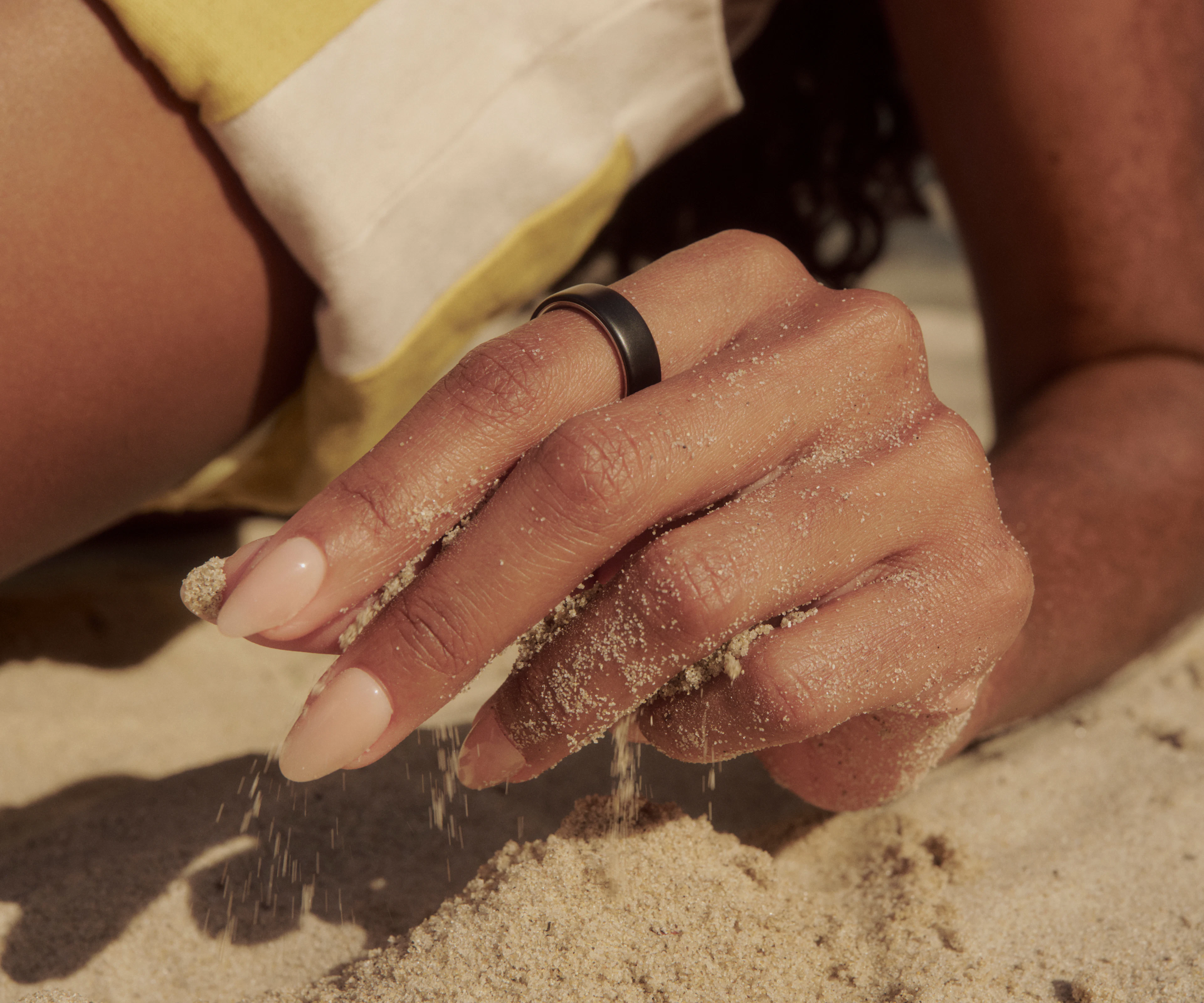 Close up of a person with their hand in the sand while wearing a Stealth Oura Ring 5.