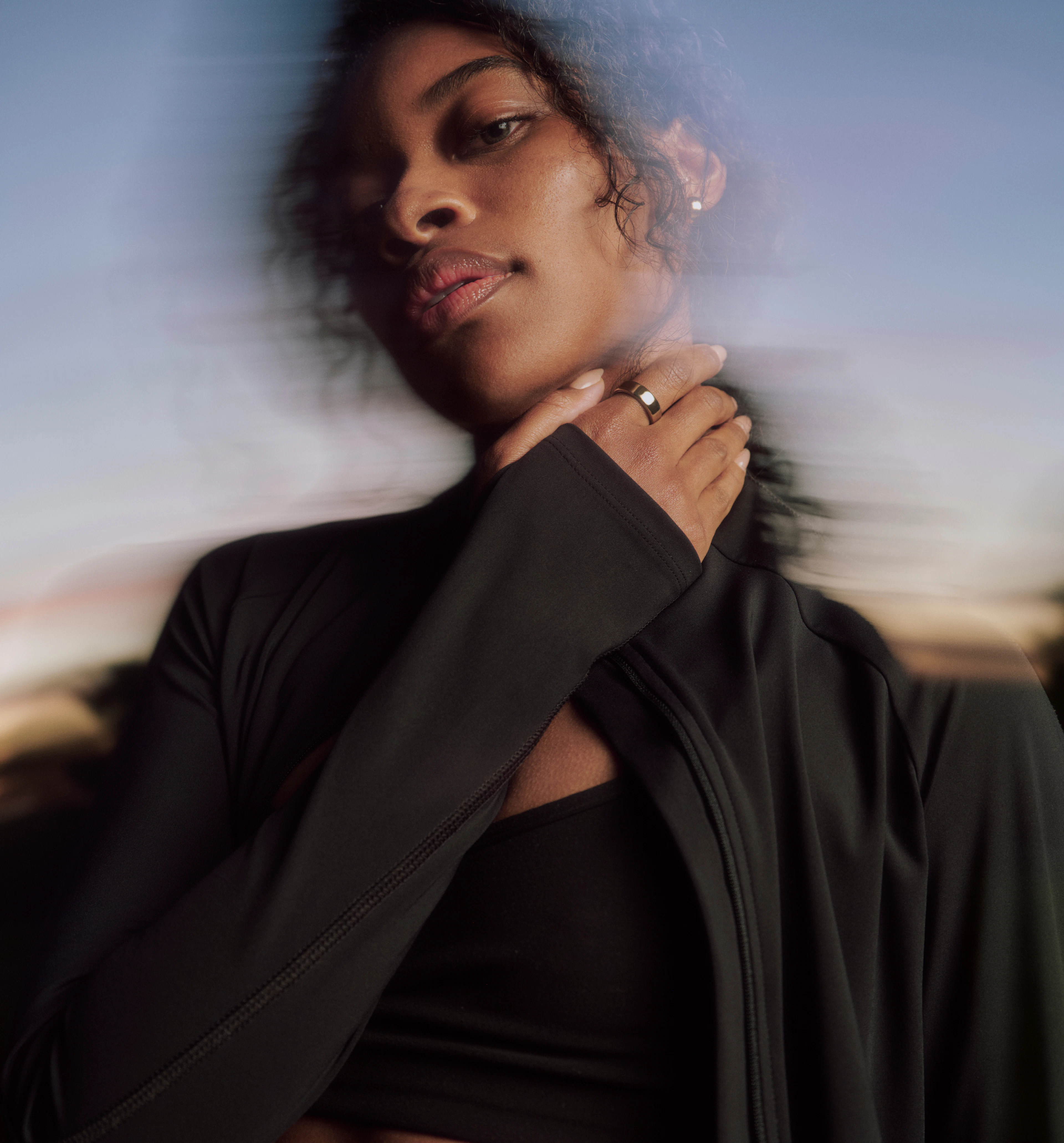 A woman gazes towards the camera while wearing an Oura Ring 5 in Gold finish