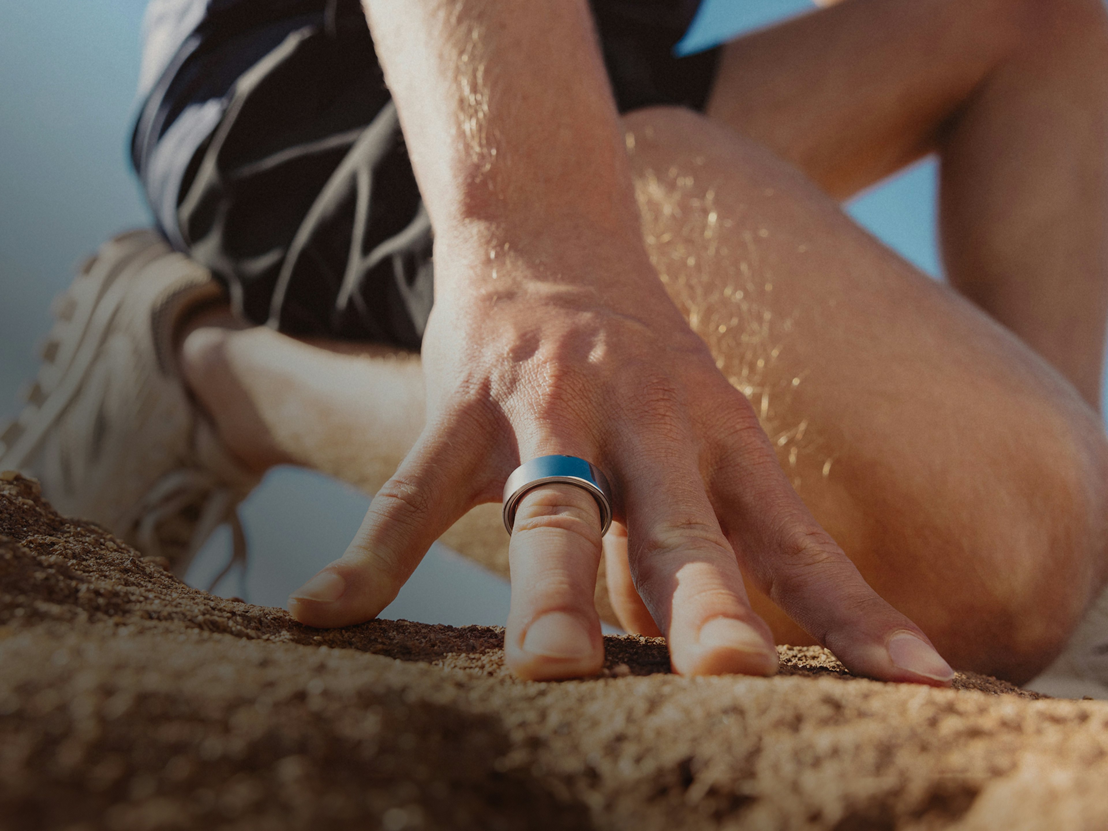 砂地の地面に膝をつくOura Ring 4を着用した男性