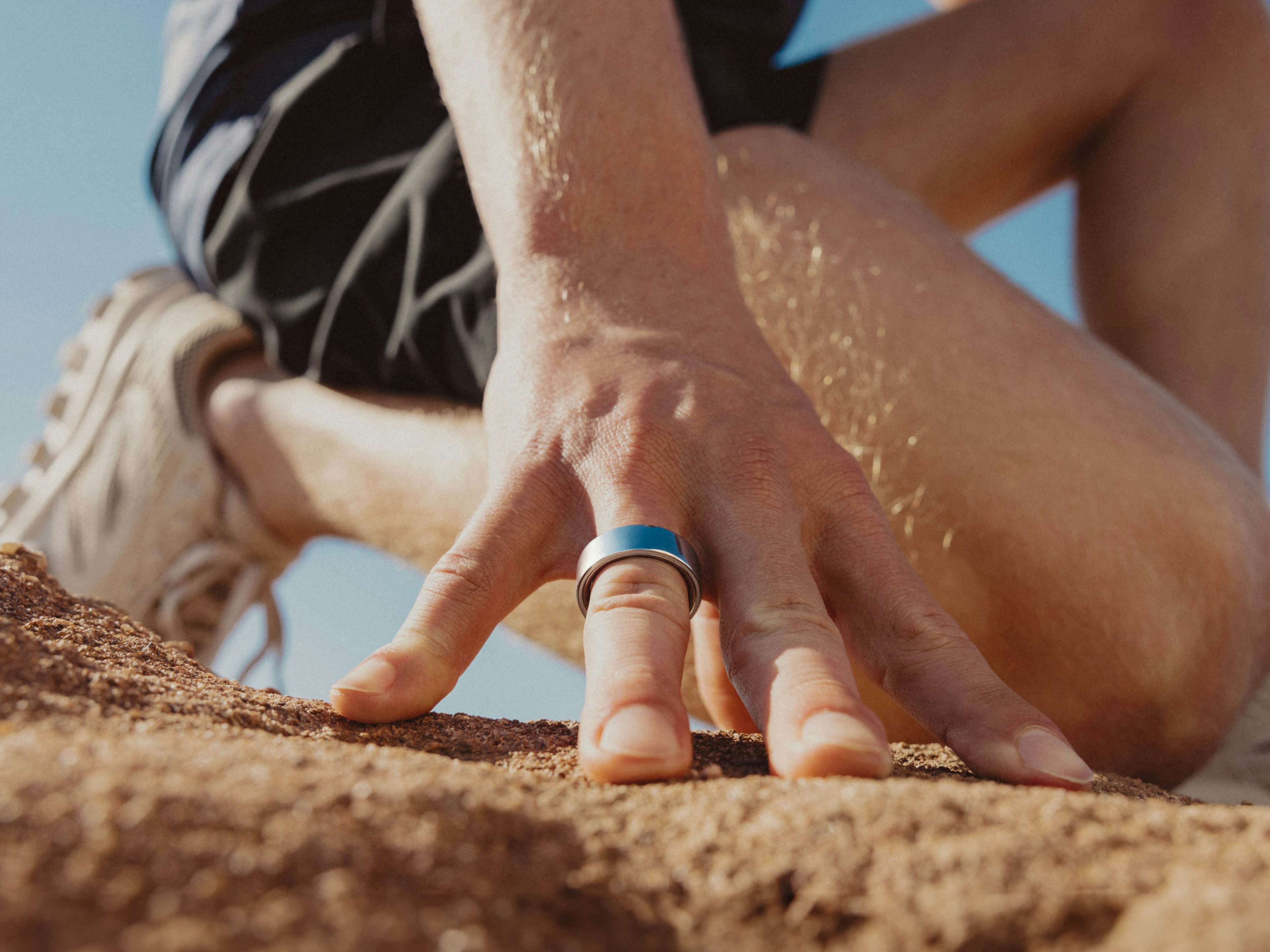 Mann trägt Oura Ring 4 und kniet im Sand
