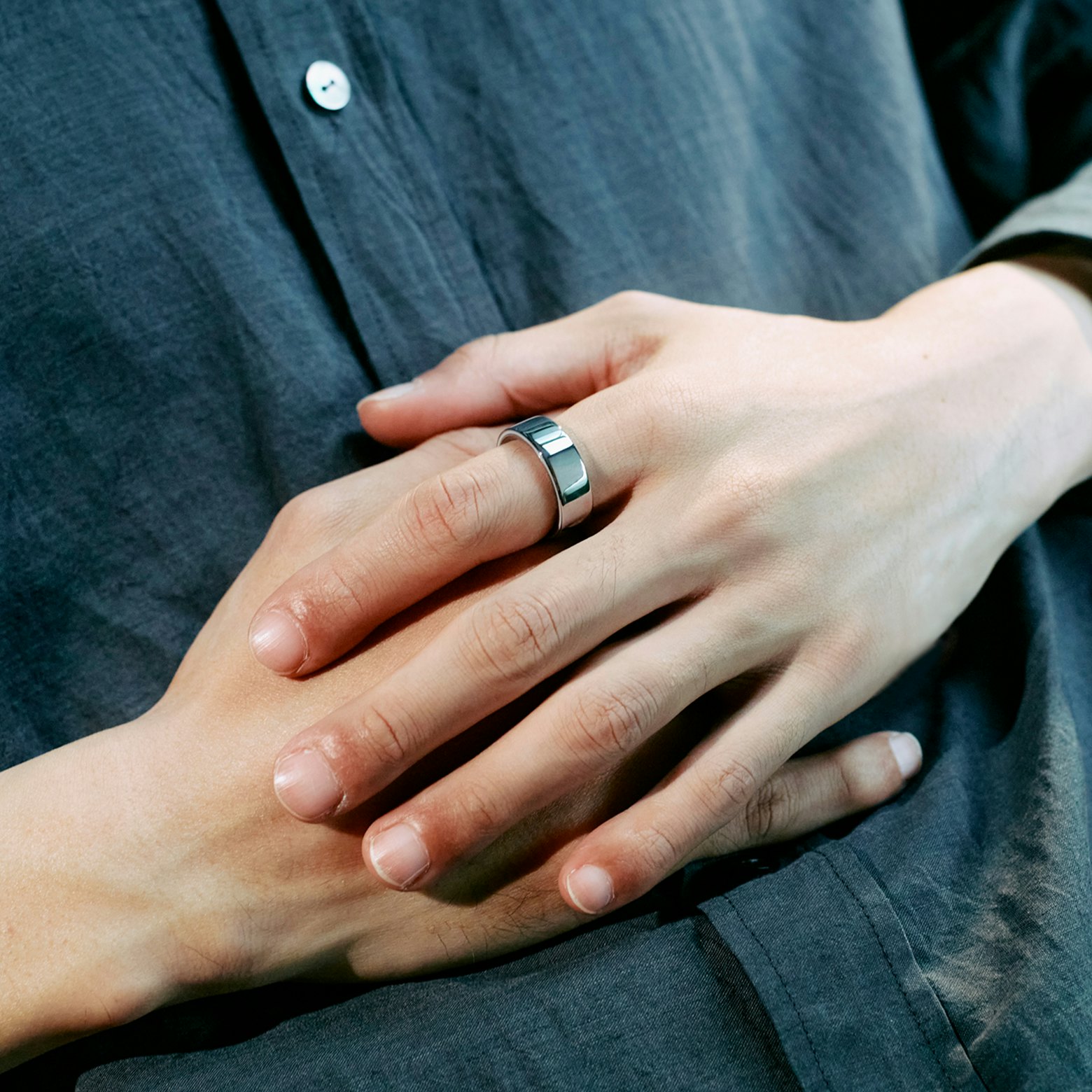 A close-up shot of a man's hands on his belly, with an Oura Ring on his index finger.