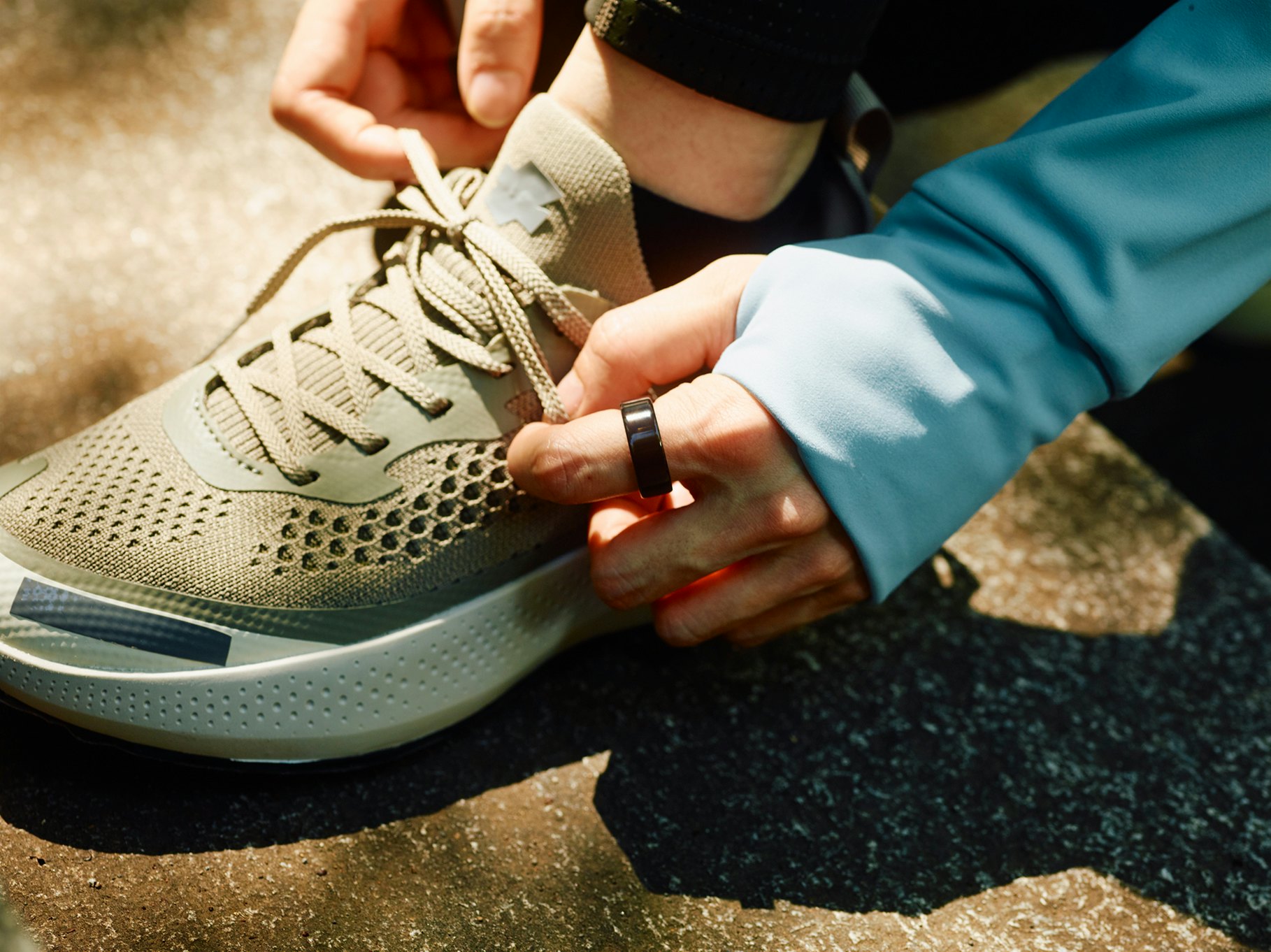 A close-up shot of a woman tying her shoe while wearing an Oura Ring on her index finger.