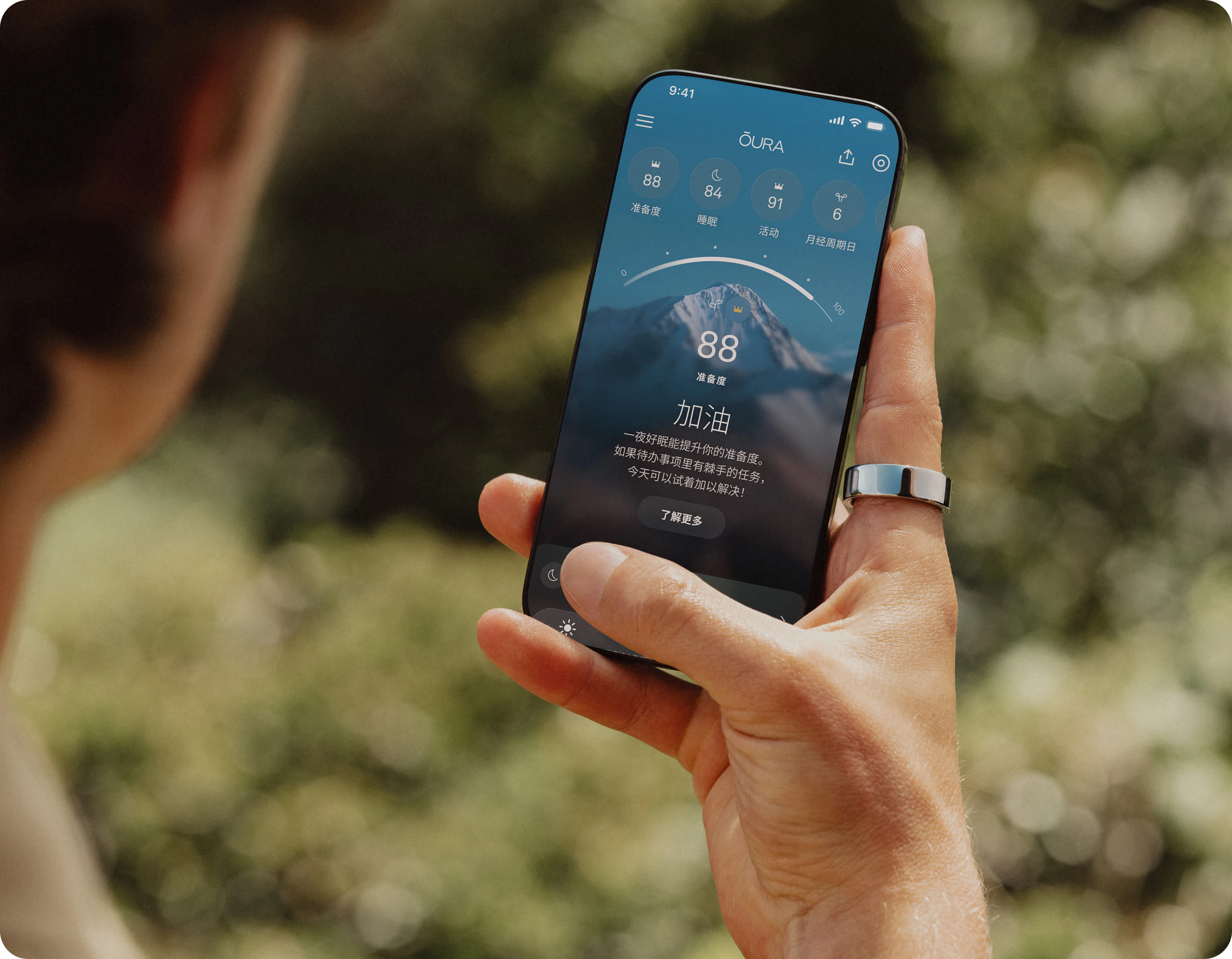 一个人右手食指佩戴着 Oura Ring,正在智能手机上查看 Oura App