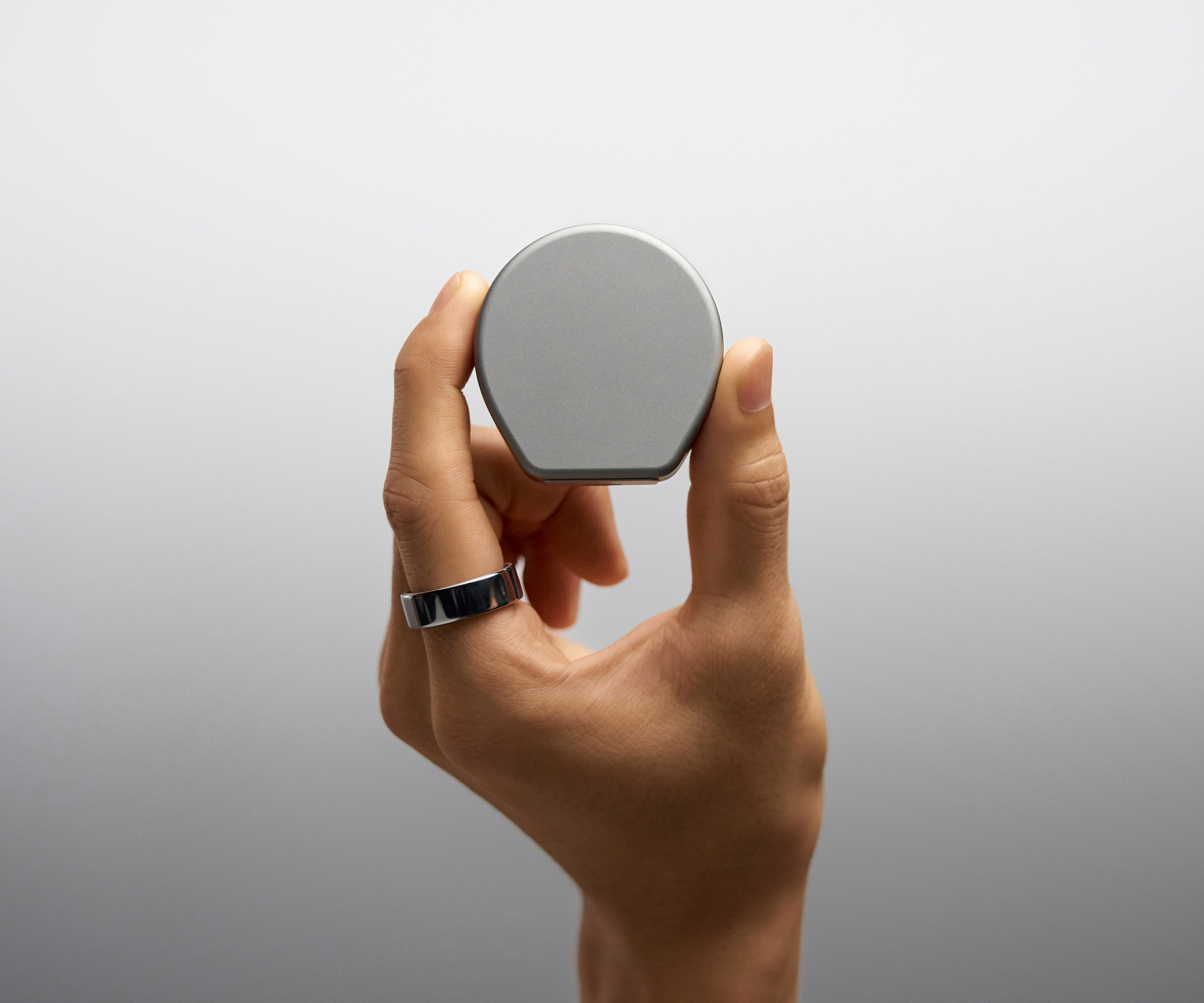 A close-up of a hand holding the Oura Ring 4 Charging Case with the lid closed.