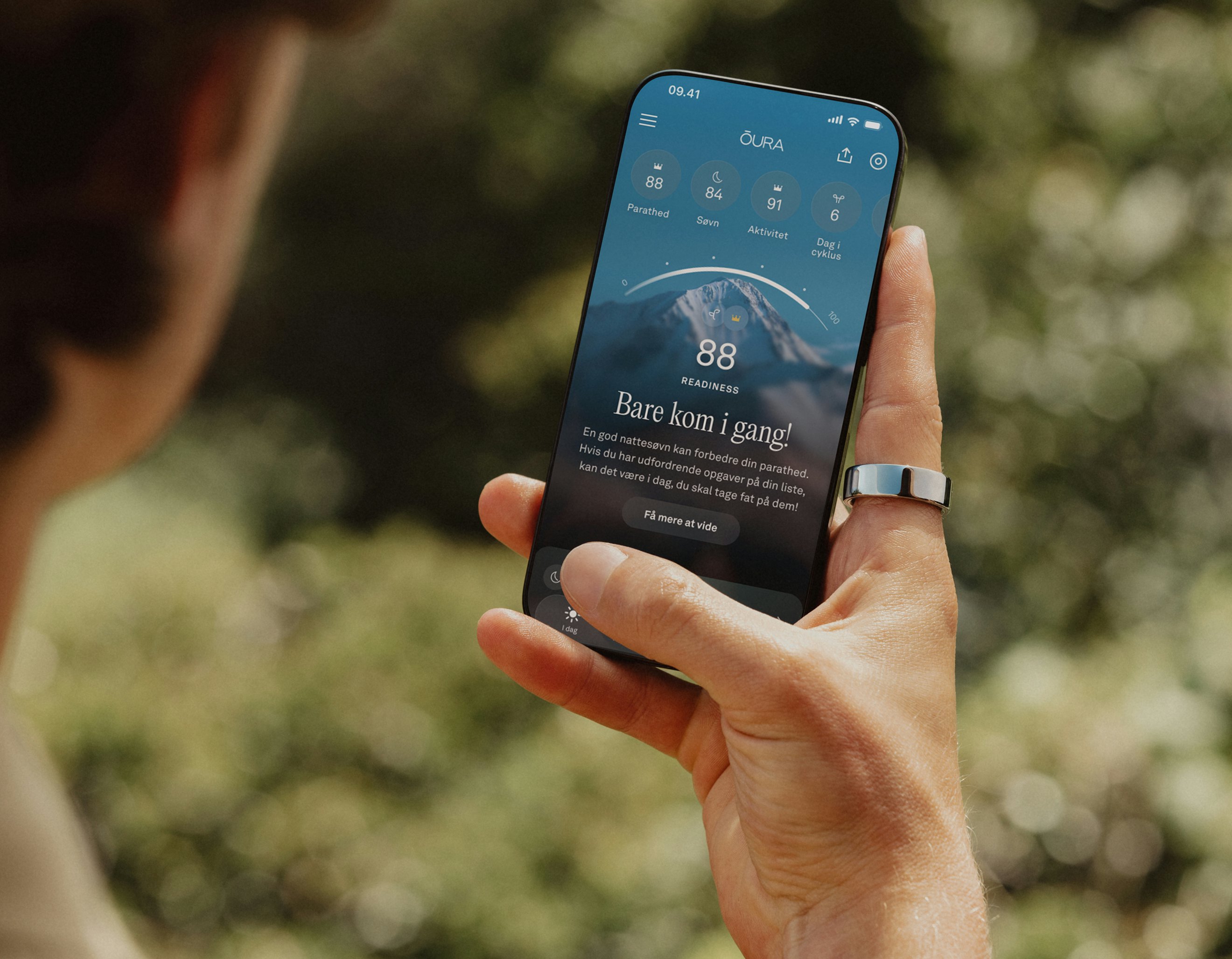 En person, der ser på Oura-appen på sin smartphone og har en Oura Ring på højre pegefinger