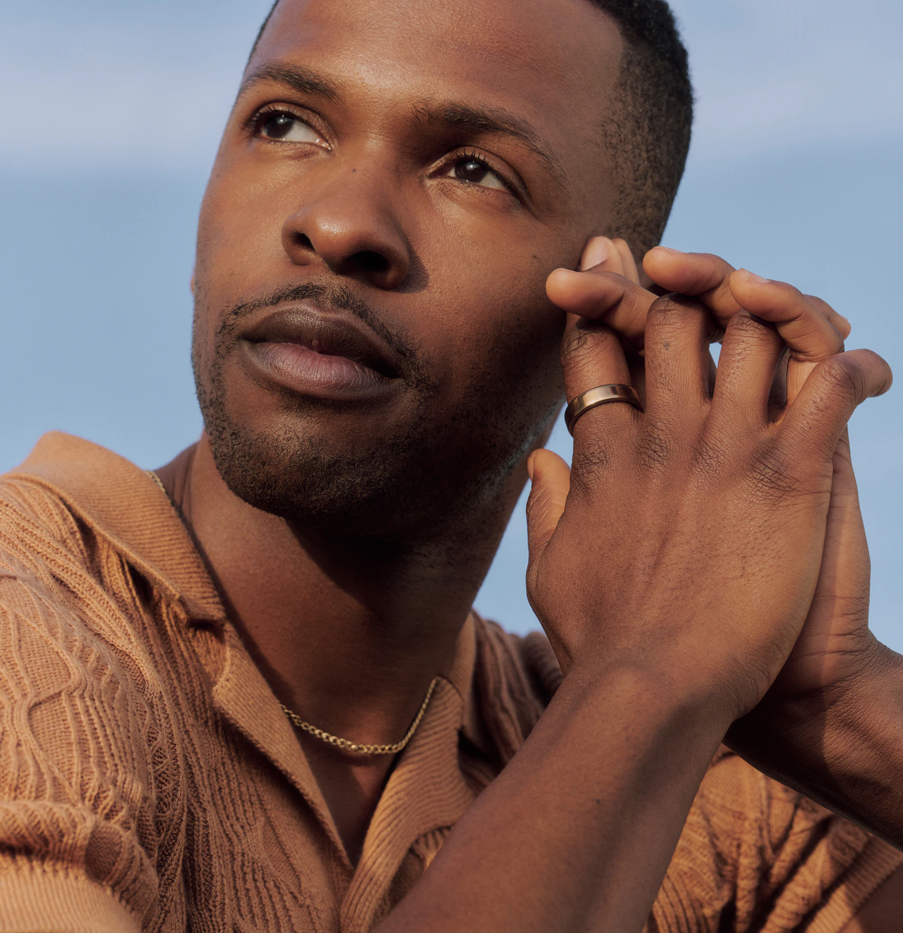 A person looking upward with hands clasped near their face, wearing an Oura Ring on their index finger.