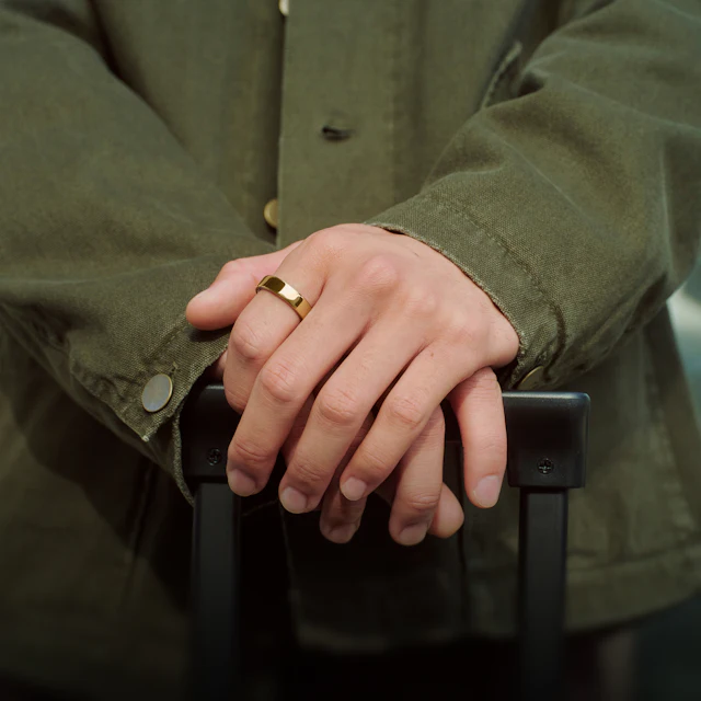 Close up of a person's hands resting on the handle of a suitcase with a Gold Oura Ring 5 on their finger